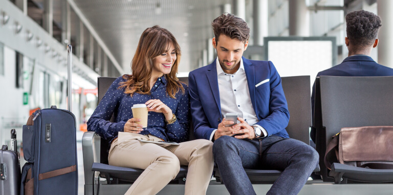 Couple sitting at airport using mobile phone