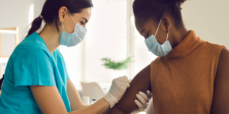 masked nurse giving vaccination to woman